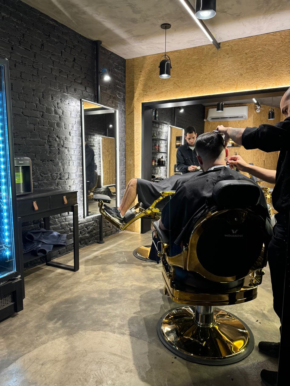 Ambiente real da Barbearia Pamplona, com paredes de tijolos escuros, espelhos iluminados e poltronas com detalhes dourados